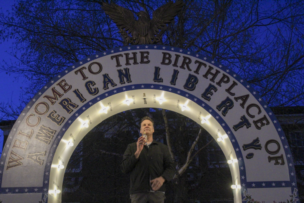 A man holding the final lightbulb to fully light up the VO-250 Arch.